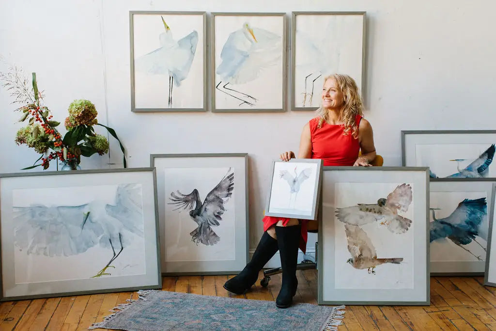 Holly Wach (artist) sitting in a chair holding her original bird watercolor art