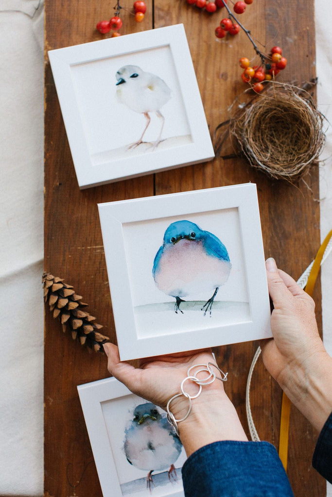 a watercolor artist holding a framed picture of a bird