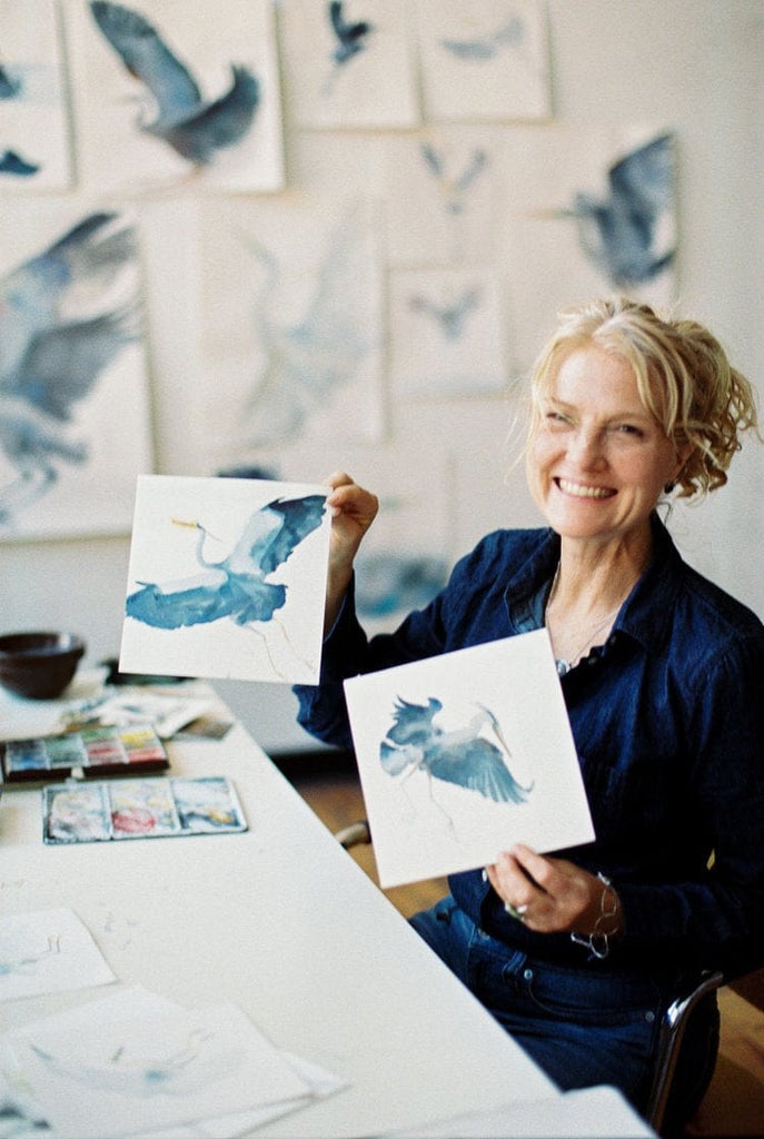 Holly Wach (artist)  sitting in a chair holding her original bird watercolor art