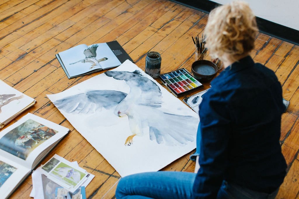 Holly is sitting on the floor painting bird watercolor art