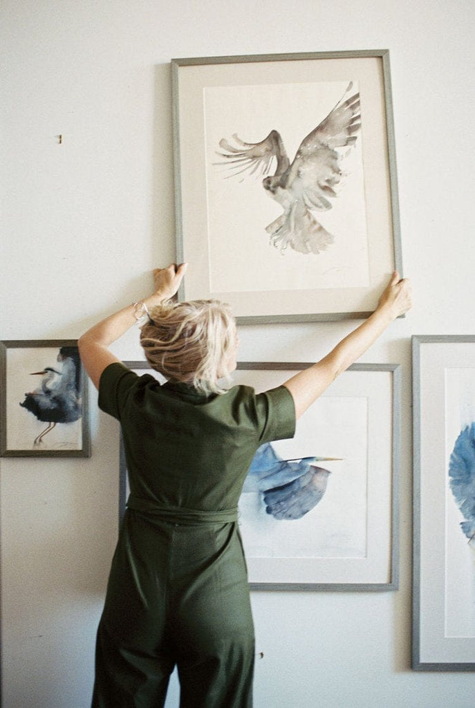 Holly standing in front of a wall with her original bird watercolor art