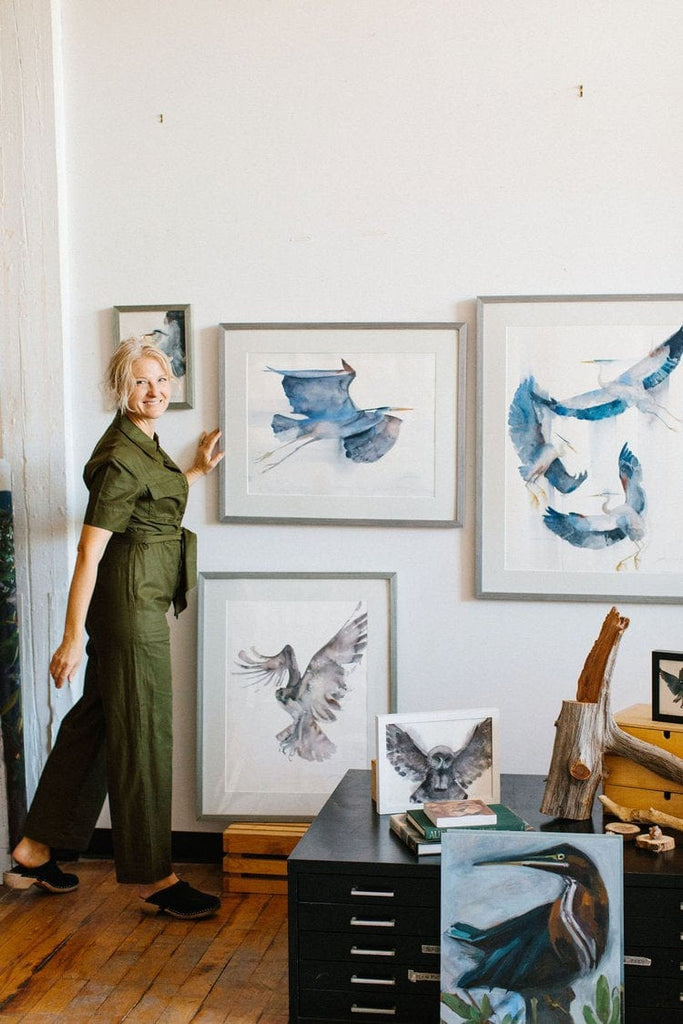 Holly Wach (artist) standing in front of a wall showing her original bird art watercolor