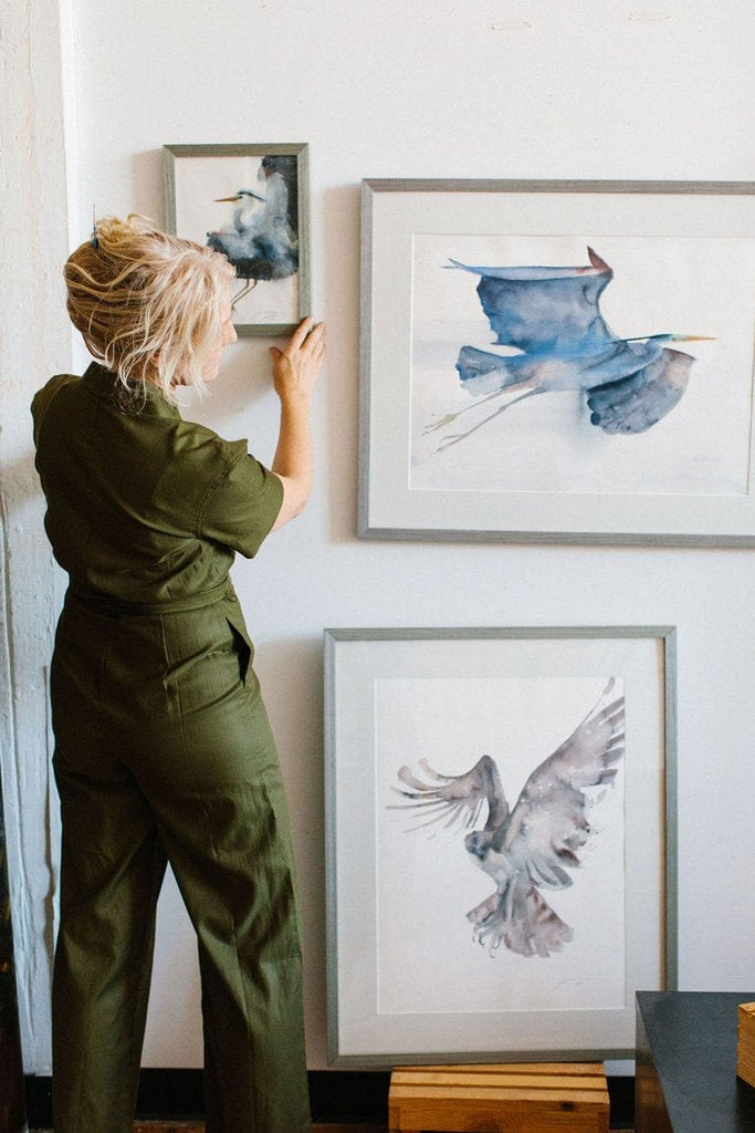 Holly Wach (artist) standing in front of a wall with her original paintings