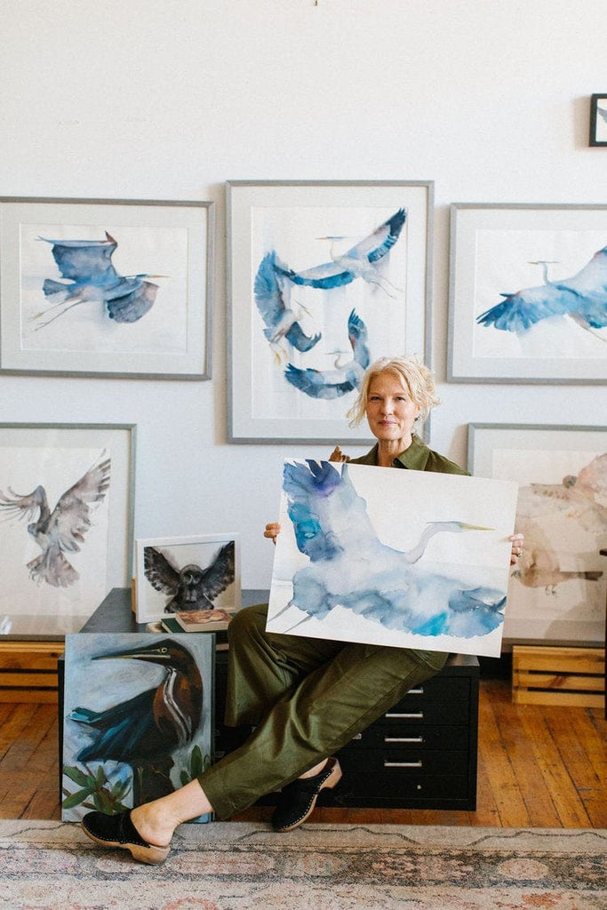 Holly Wach (artist)  sitting in a chair holding her original bird watercolor art