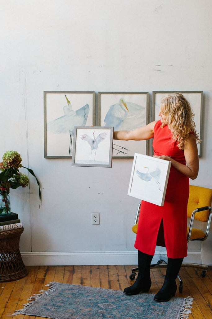 Holly Wach (artist) standing in front of a wall with her bird watercolor art
