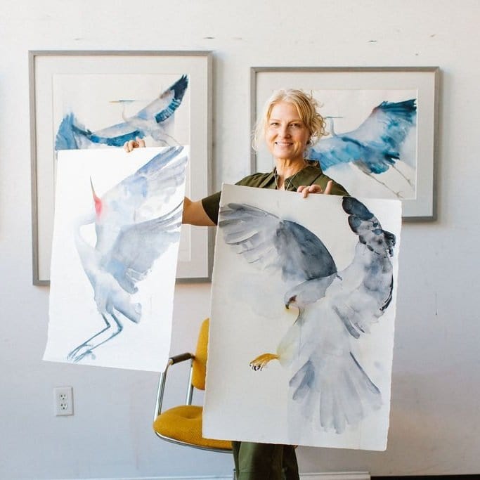 Holly Wach standing in her studio with her bird watercolor art